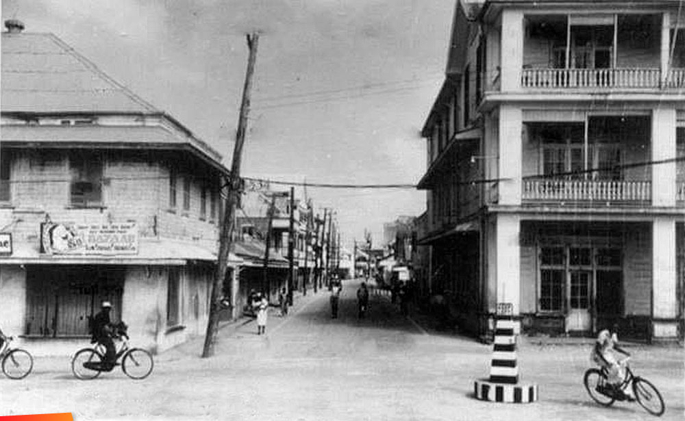 Bicycles and foot traffic on Queen Street, Belize, British Honduras, long ago