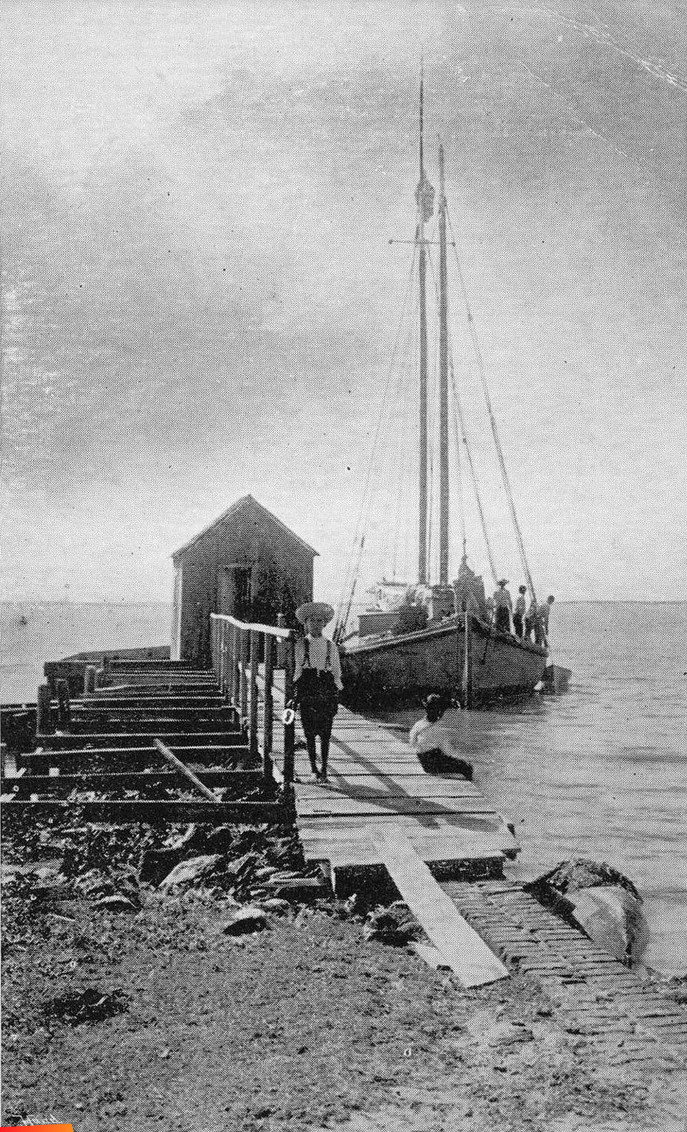 Scene on the coast of British Honduras, several folks and their boat alongside a pier, long ago